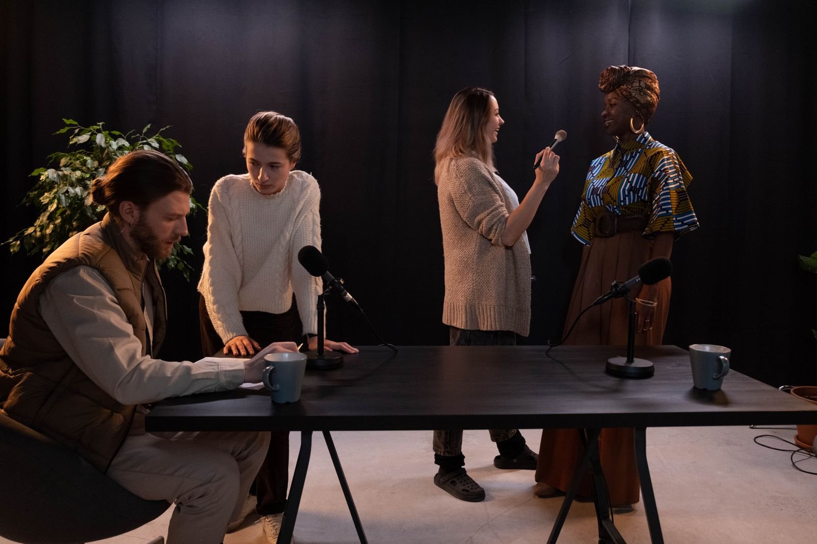 Plusieurs personnes d'origines diverses autour d'une table de studio équipée de micros avant un enregistrement