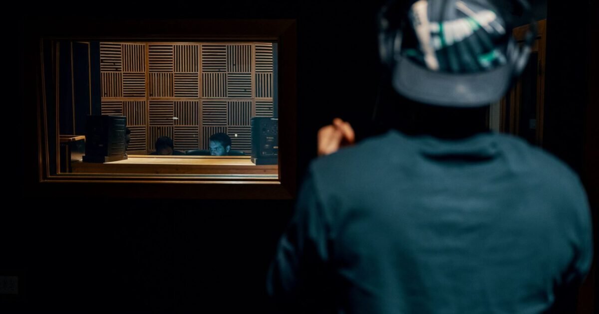 Ingénieur du son en régie, casque sur les oreilles, face à la cabine d'enregistrement
